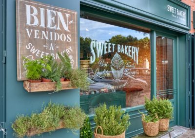 SWEET BAKERY, el obrador clásico inglés. En pleno barrio de Montequinto, siendo una antigua tienda de chucherías… Surge una imponente fachada verde carruaje completamente de madera y cristal, al más puro estilo ingles clásico. El diseño de un gran escaparate pintado a mano.Sweet Bakery es un pequeño obrador artesanal donde se elaboran grandes tartas, pasteles y cupcakes entre otros… Un diseño que destaca sobre la fachada de un edificio actual. Con puertas de hierro que se abren y adornadas con plantas y cestos de mimbre.Todo un concepto natural, artesanal y clásico con paredes de ladrillo antiguo, moldurones, zócalos. Un suelo hidráulico gastado con bancos y tapas de madera vieja, nos transporta 100 años atrás. Incluyendo una carpintería que nos permite ver el trabajo que se realiza de obrador en su interior.