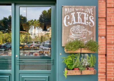 SWEET BAKERY, el obrador clásico inglés. En pleno barrio de Montequinto, siendo una antigua tienda de chucherías… Surge una imponente fachada verde carruaje completamente de madera y cristal, al más puro estilo ingles clásico. El diseño de un gran escaparate pintado a mano.Sweet Bakery es un pequeño obrador artesanal donde se elaboran grandes tartas, pasteles y cupcakes entre otros… Un diseño que destaca sobre la fachada de un edificio actual. Con puertas de hierro que se abren y adornadas con plantas y cestos de mimbre.Todo un concepto natural, artesanal y clásico con paredes de ladrillo antiguo, moldurones, zócalos. Un suelo hidráulico gastado con bancos y tapas de madera vieja, nos transporta 100 años atrás. Incluyendo una carpintería que nos permite ver el trabajo que se realiza de obrador en su interior.