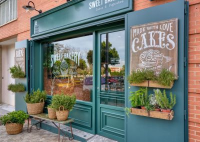 SWEET BAKERY, el obrador clásico inglés. En pleno barrio de Montequinto, siendo una antigua tienda de chucherías… Surge una imponente fachada verde carruaje completamente de madera y cristal, al más puro estilo ingles clásico. El diseño de un gran escaparate pintado a mano.Sweet Bakery es un pequeño obrador artesanal donde se elaboran grandes tartas, pasteles y cupcakes entre otros… Un diseño que destaca sobre la fachada de un edificio actual. Con puertas de hierro que se abren y adornadas con plantas y cestos de mimbre.Todo un concepto natural, artesanal y clásico con paredes de ladrillo antiguo, moldurones, zócalos. Un suelo hidráulico gastado con bancos y tapas de madera vieja, nos transporta 100 años atrás. Incluyendo una carpintería que nos permite ver el trabajo que se realiza de obrador en su interior.